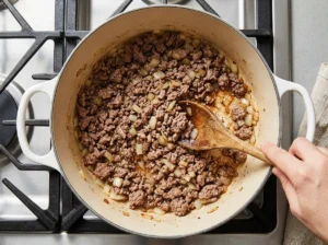 Browning ground beef and diced onion in a white Dutch oven for taco soup