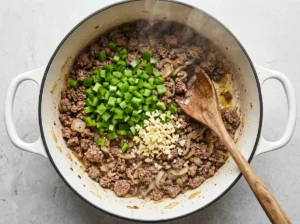 Green bell pepper and garlic added to browned ground beef in a Dutch oven
