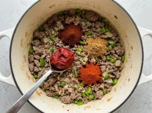 Tomato paste and taco spices added to ground beef in a Dutch oven