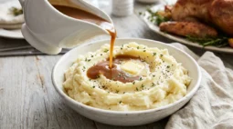 Turkey gravy for mashed potatoes pouring from a white gravy boat into a buttery mashed potato well